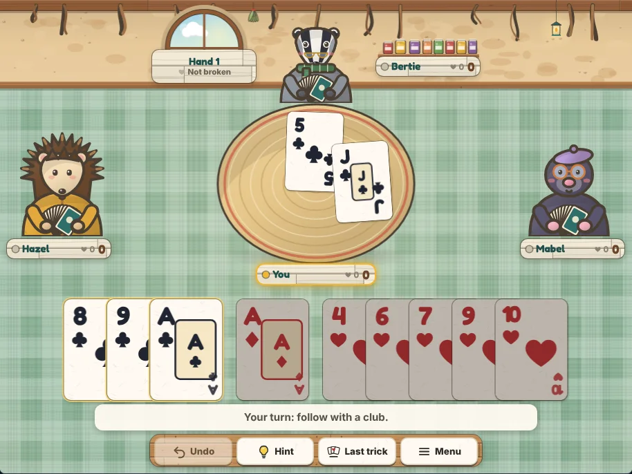 Actual Kettle Burrow Hearts gameplay on a desktop browser: the burrow kitchen with Hazel the hedgehog on the left, Bertie the badger at the top and Mabel the mole on the right, each holding face-down cards and each with a name plate showing their score and points this hand, a trick in progress on a woven mat in the middle, your hand of cards along the bottom sorted by suit with the cards you may play outlined and the others dimmed, a hand sign showing whether hearts are broken, and Undo, Hint, Last trick and Menu on the shelf below.